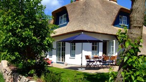 Ein Haus mit einem Strohdach, einer Steinmauer und einer Terrasse mit Gartenmöbeln.