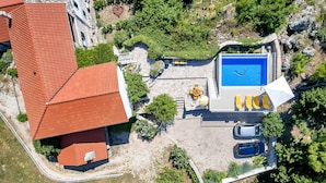 An aerial view of a property with a swimming pool, a red-roofed building, and a stone wall.