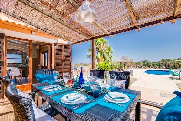 An outdoor dining area with a table set for four, surrounded by wicker chairs, under a thatched roof. - Rural Finca in Mallorca Can Frit with pool (Santa Margalida)