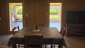 A dining area with a table set for four, wooden walls, and a television on a stand. - Ground floor apartment for rent in Bernex for 5 people (Bernex)