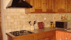 Une cuisine avec des meubles en bois, une cuisinière à gaz, un four à micro-ondes et un dosseret carrelé.