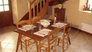 Une table à manger dressée avec des assiettes, des verres et un saladier, entourée de chaises en bois.