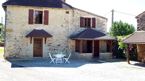 Un bâtiment en pierre avec un toit en pente, des volets en bois et un petit espace extérieur aménagé avec une table et des chaises.