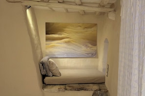 A narrow room with a bed, a painting on the wall, and a window.