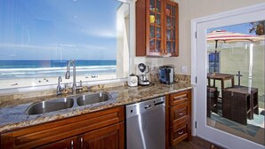 Une cuisine avec vue sur la plage, des meubles en bois, un lave-vaisselle et une machine à café.
