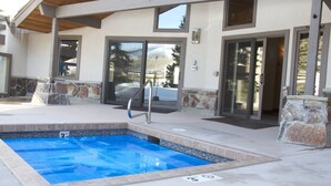 Zona de piscina con borde de piedra, escalera metálica y un porche cubierto.