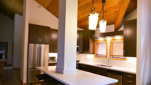 Una cocina moderna con armarios oscuros, encimera blanca y una lámpara colgante.