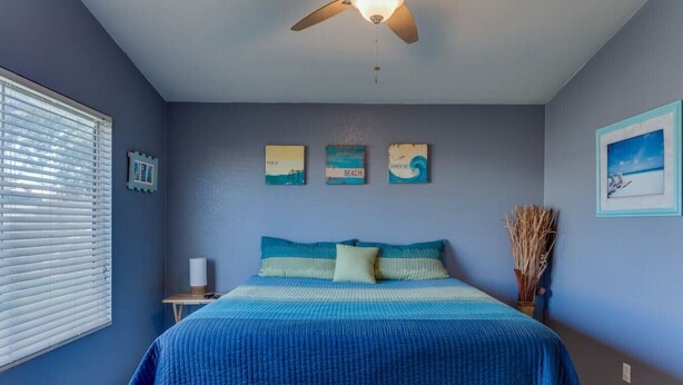 Quarto com cama, ventoinha no teto e quadros nas paredes.