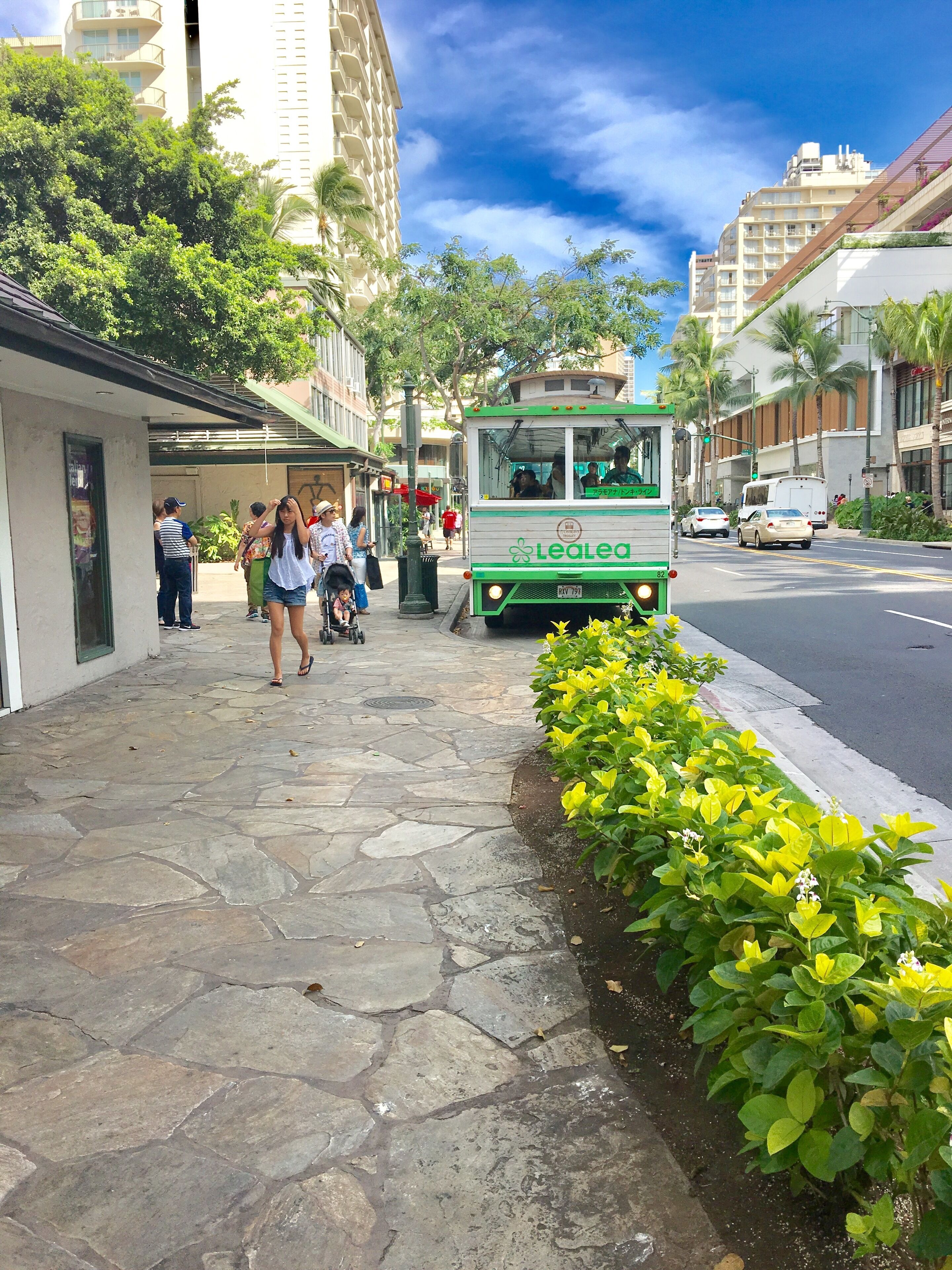A street scene with a green and white tram, pedestrians, and buildings.
