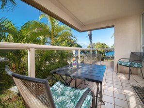 A balcony with a table and chairs, overlooking a pool and palm trees.