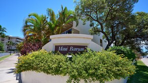 A sign for "Maui Banyan" with a white building and lush greenery in the background.