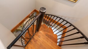 Un escalier en colimaçon en bois, doté d’une main courante en métal et d’une rampe en métal noir.