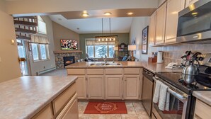 A modern kitchen with a central island, stainless steel appliances, and a stone fireplace. - Tyra Streamside Wolf’s Lair Condo: Ski-In/Ski-Out (Breckenridge)