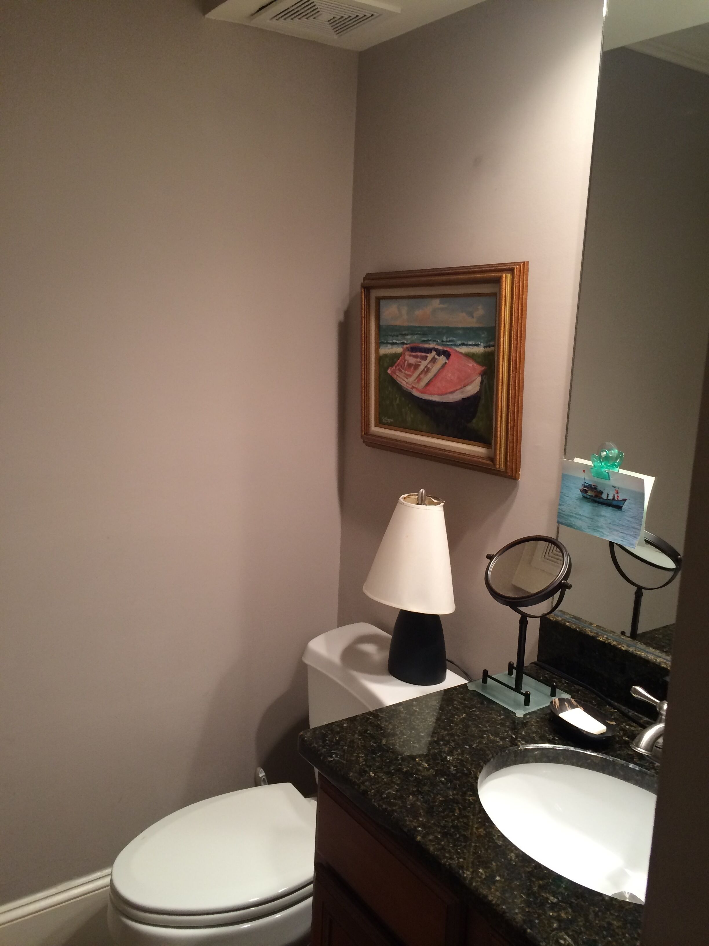 Une salle de bain avec des toilettes, un lavabo et un tableau encadré représentant un bateau, accroché au mur.