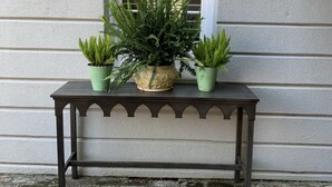 A stone-paved patio with a black metal table holding three potted plants and a decorative vase.
