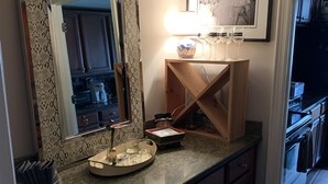 A kitchen with a large mirror, wooden cabinets, a countertop with a tray of glasses, and a framed photograph on the wall.