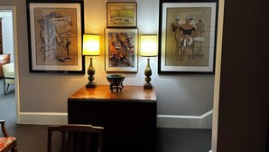 A hallway with framed artwork on the walls, a wooden table with a bowl, and two lamps.