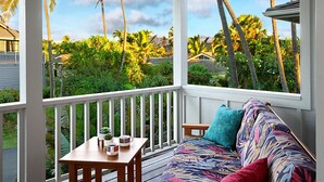 Eine überdachte Veranda mit Holztisch und -stühlen, einer Couch mit Kissen und Blick auf tropische Vegetation sowie Häuser.