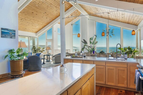 A modern kitchen with wooden cabinets, a marble countertop, and large windows offering ocean views. - Incredible Ocean Front Home with 3 Master Suites and Secluded Beach (Dillon Beach)
