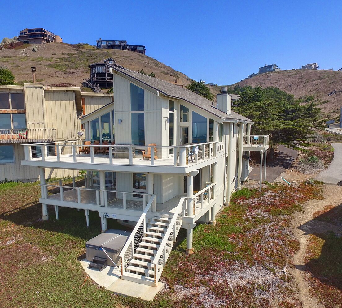 Una casa costera de varios pisos con un balcón y una escalera que conduce a la parte superior, con vistas a las colinas circundantes.