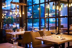 Un interior de restaurante con mesas dispuestas para comer, lámparas colgantes y amplias ventanas que ofrecen vistas al exterior.