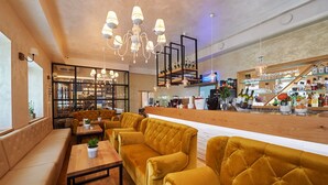 A modern bar area with yellow upholstered seating, a wooden counter, and a variety of bottles and glasses on display. - Hiša Ančka, Boutique Hotel (Slovenj Gradec)