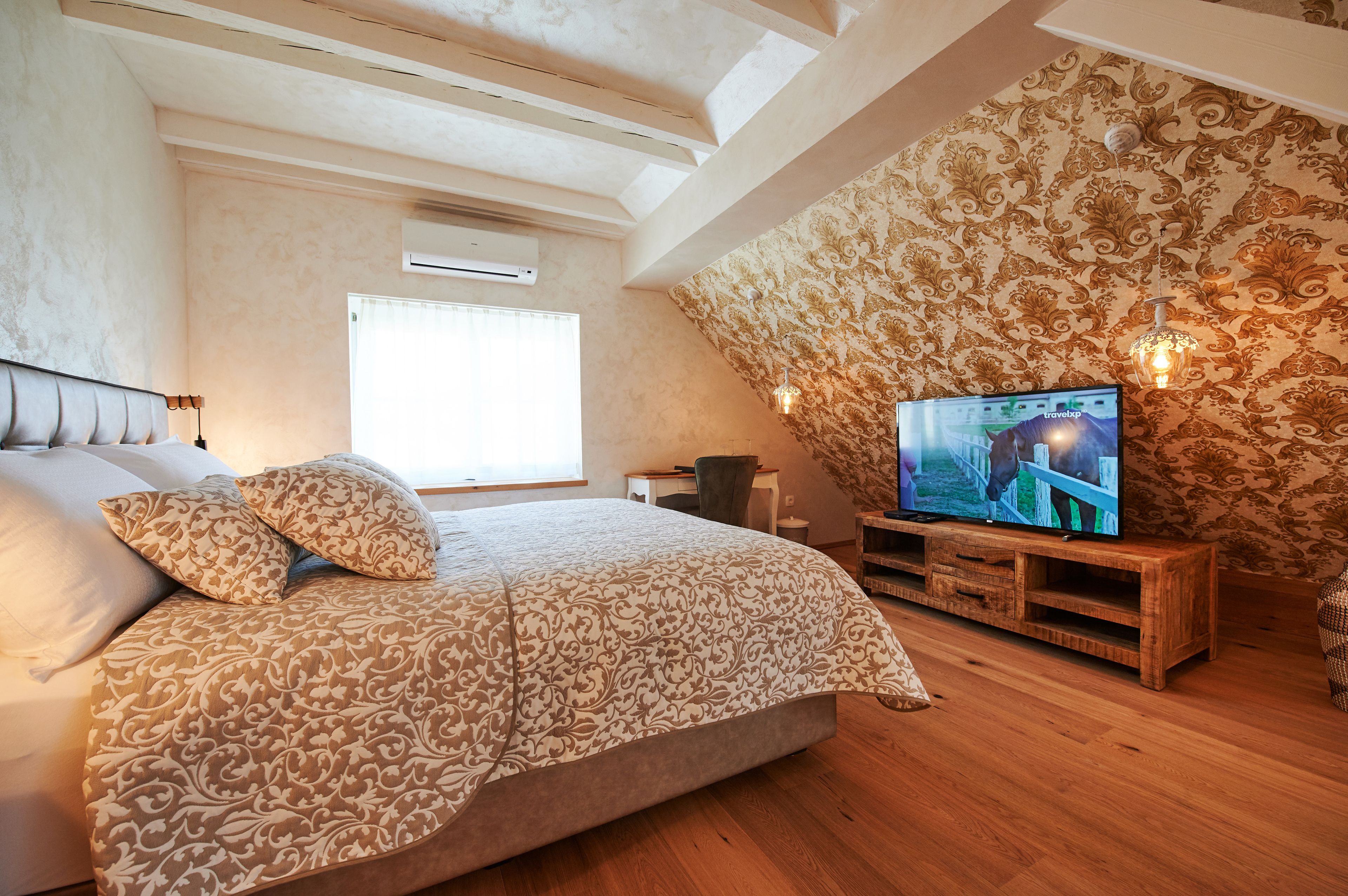 Quarto com uma cama grande, uma televisão sobre um suporte de madeira e papel de parede estampado.