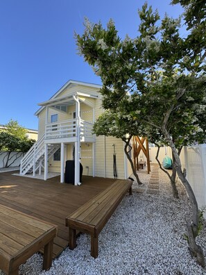 Une maison avec une terrasse en bois, un escalier menant à une zone abritée et un arbre aux fleurs blanches.