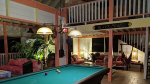 Una mesa de billar en una habitación con una hamaca colgante, un sofá y un letrero que dice "BLACK PEARL".
