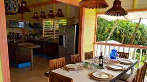 Una cocina con isla central, una zona de comedor con mesa dispuesta para seis personas, y vistas a vegetación exuberante.