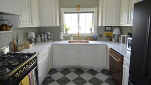 A kitchen with white cabinets, a black stove, a sink with gold faucets, and a checkered floor. - Beautifully restored Victorian Mountain home furnished with authentic antiques! (Silverton)