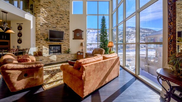Un salón espacioso con chimenea de piedra, ventanas grandes y vistas a un paisaje nevado.