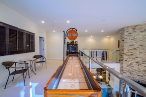 Ett shuffleboard-bord i en modern inomhusmiljö med en digital resultattavla, sittområde och en trappa.