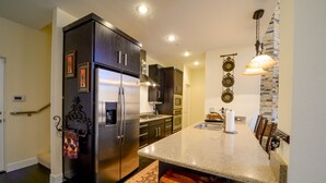 Una cocina moderna con armarios oscuros, electrodomésticos de acero inoxidable, encimera de granito y una zona de comedor con sillas de madera.