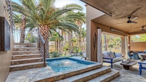 Un área de piscina con escalones que conducen a un jacuzzi, rodeado de palmeras y un patio con mobiliario exterior.