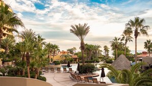 Área de piscina en un resort con sillones de descanso, palmeras y vista al océano.