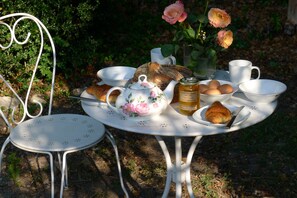A round white table with a floral teapot, cups, a basket of bread, a jar of jam, and a croissant. - Beautifully Restored, Large French Villa On The Banks Of The River Cele. (Cabrerets)