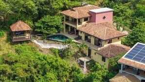 Una amplia casa de varios pisos con piscina, rodeada de abundante vegetación.