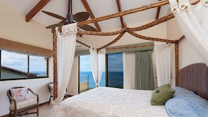 Un dormitorio con una cama grande, ventilador de techo y vista al océano.