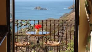 Un balcón con una mesa y dos sillas, con vista al mar y una pequeña isla.
