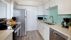 Eine moderne Küche mit weißen Schränken, einem Edelstahlkühlschrank, einer Mikrowelle und einem Waschbecken mit grüner Spritzschutzwand.