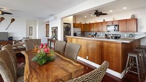 A modern kitchen with wooden cabinets, a central island, and bar stools. - Hale Nalu - Beachfront Home Steps from Baby Beach with Spa/AC! (Koloa)