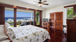 A bedroom with a bed, a ceiling fan, a TV, and a view of the ocean. - Hale Nalu - Beachfront Home Steps from Baby Beach with Spa/AC! (Koloa)