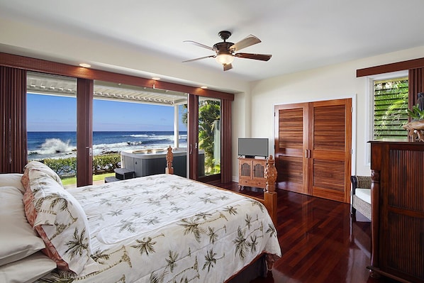 A bedroom with a bed, a ceiling fan, a TV, and a view of the ocean.