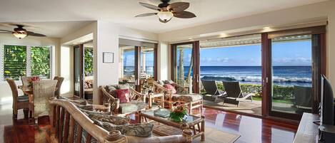 A spacious living area with a view of the ocean, furnished with wooden furniture and a ceiling fan.
