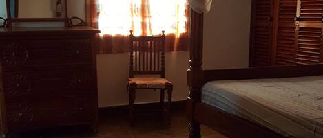Un dormitorio con una cama de madera, un aparador de madera, una silla y una ventana con cortinas.