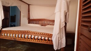 Una cama con estructura de madera y ropa de cama blanca, una puerta de madera con manija y una pared azul de fondo.
