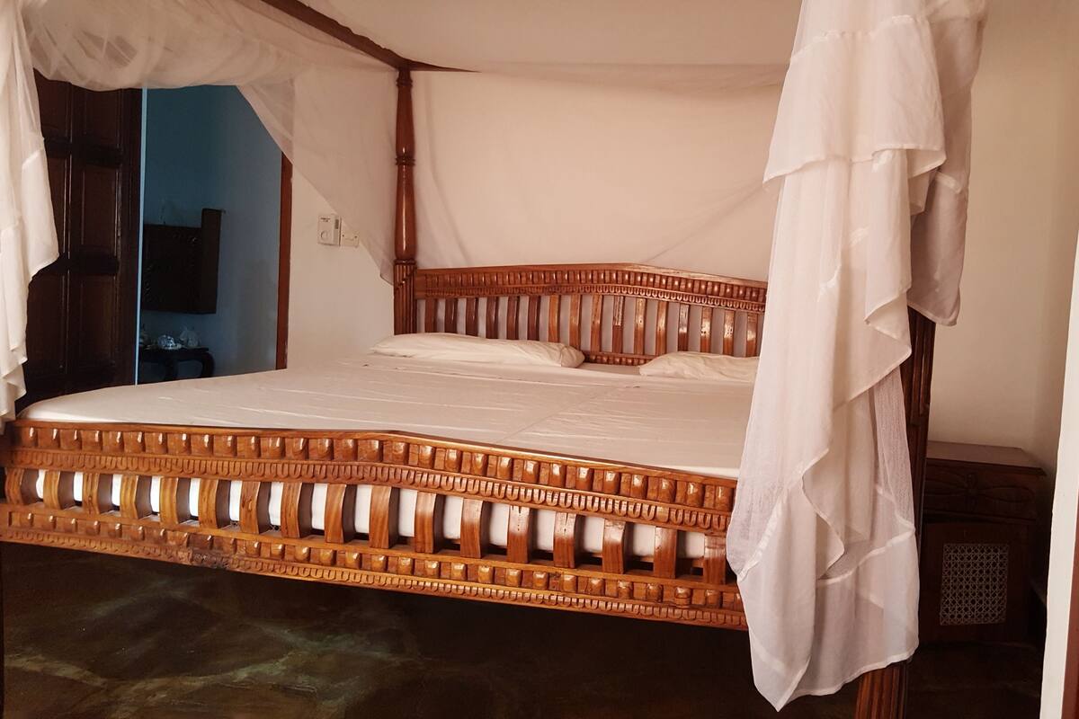 A bed with a wooden frame and white bedding, a wooden door with a handle, and a blue wall in the background.