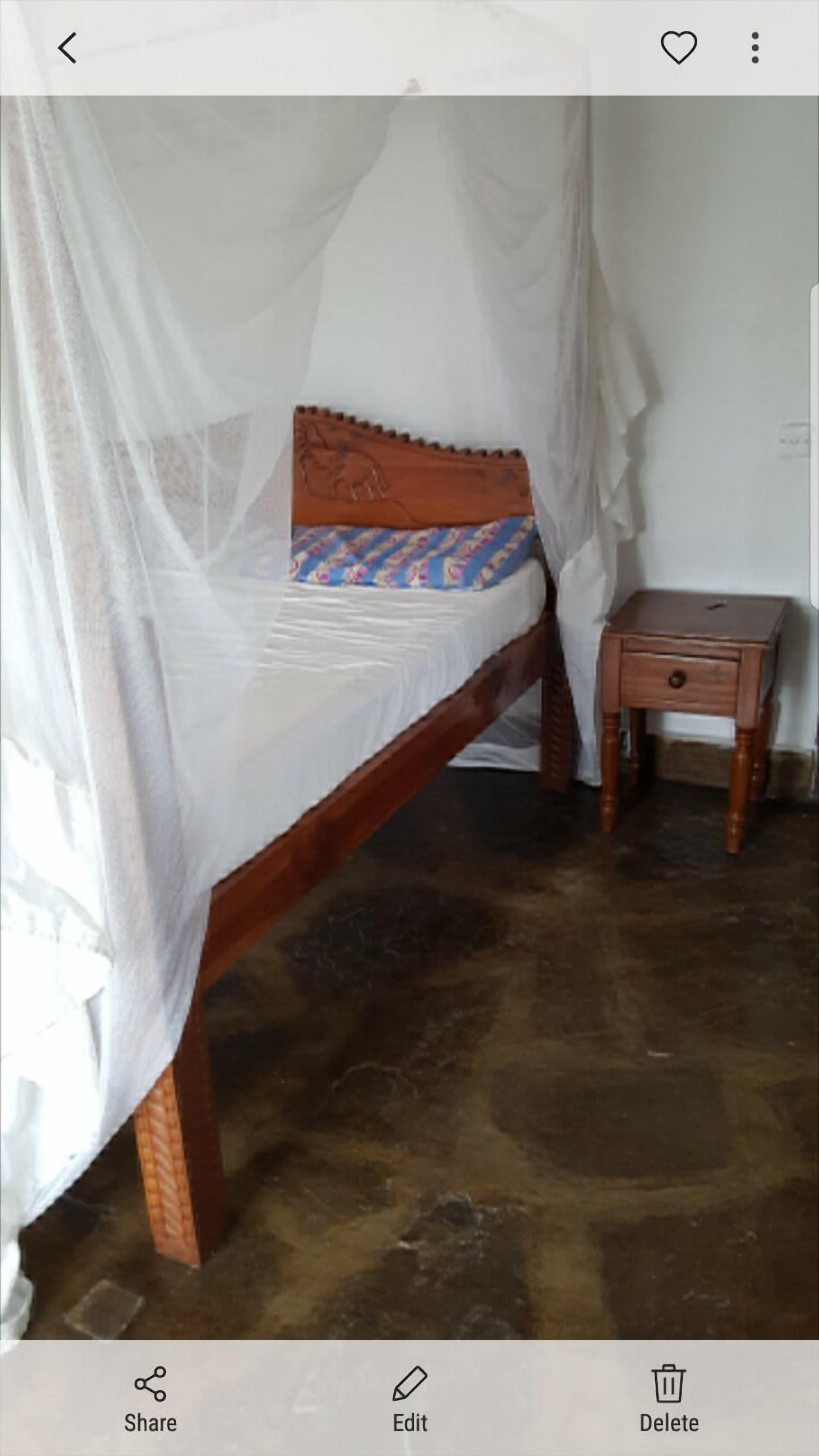 A bed with a wooden frame and a white bedspread, a small wooden nightstand beside it, and a white wall in the background.