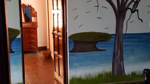 Una habitación con un mural de un árbol y pájaros, un aparador de madera y una puerta que da a otra habitación.